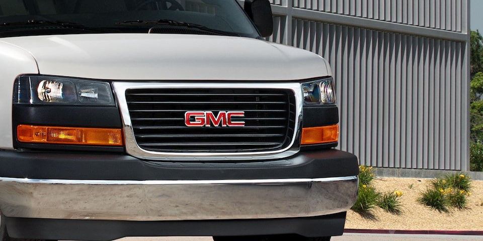 Front view of a GMC van with chrome bumper and black grille, parked near a modern building.